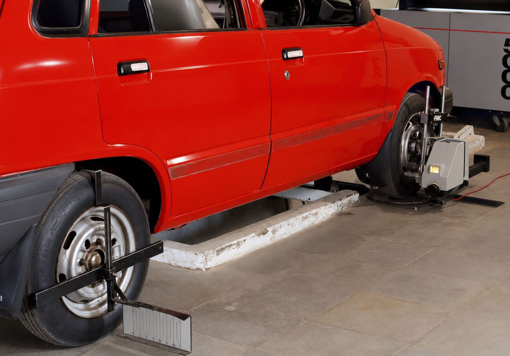 Red compact car in an automotive workshop undergoing computerized wheel alignment service.
