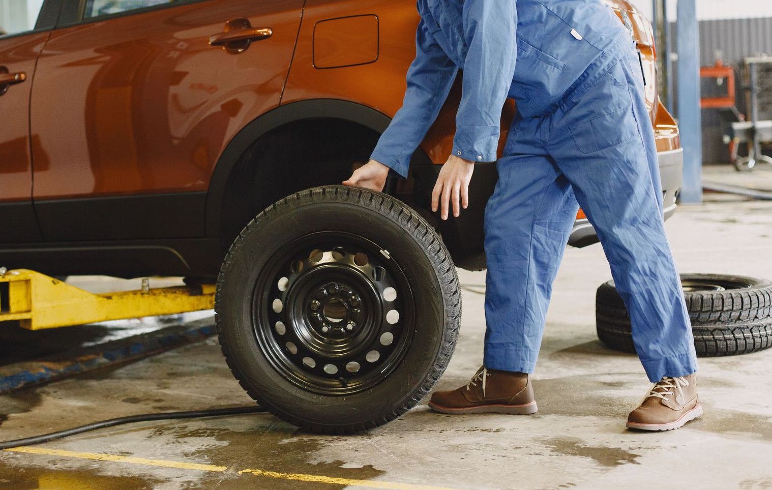 Mechanic in blue coveralls replacing tire on red SUV in repair shop garage.