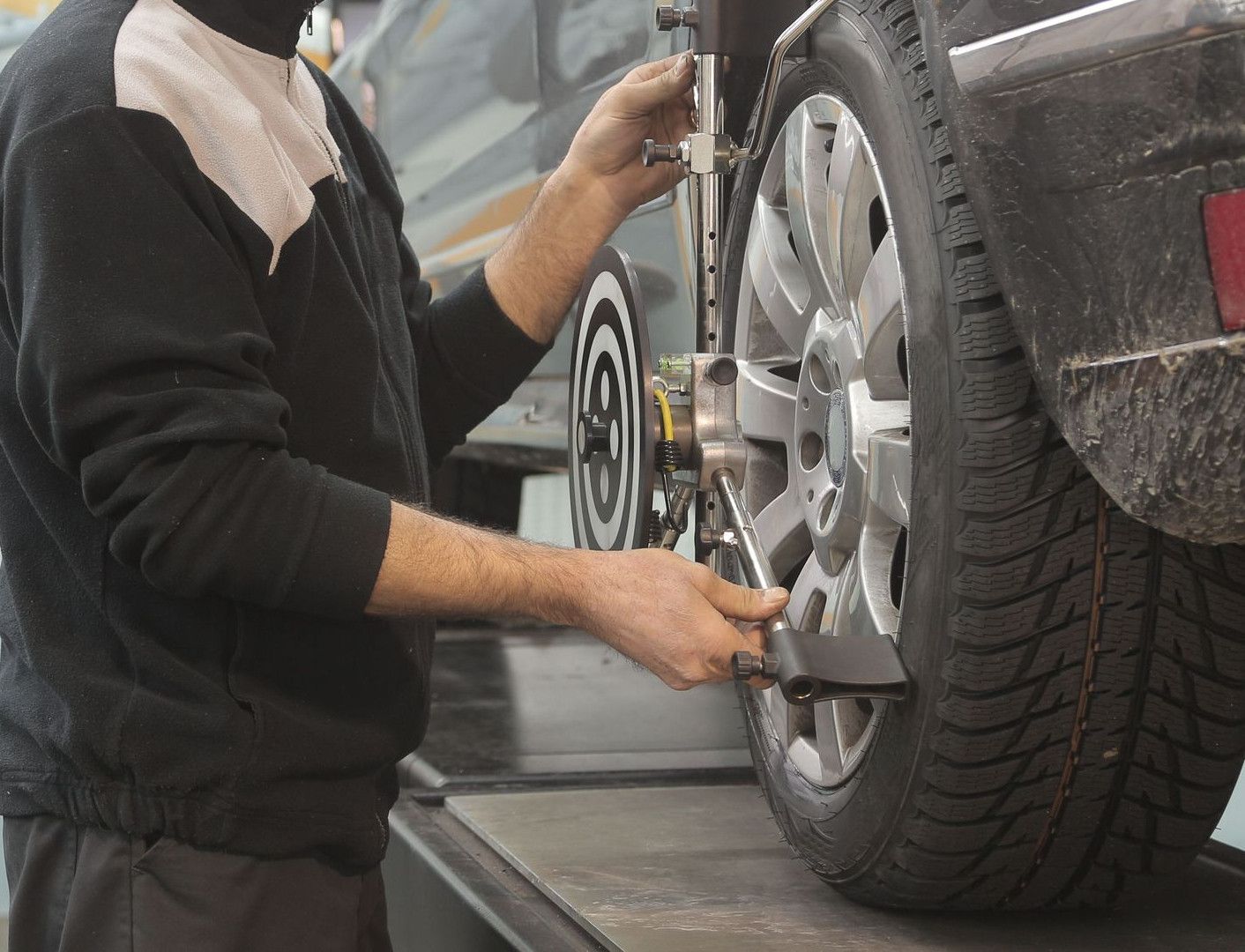 Mechanic performing wheel alignment on a car in a professional garage setting.